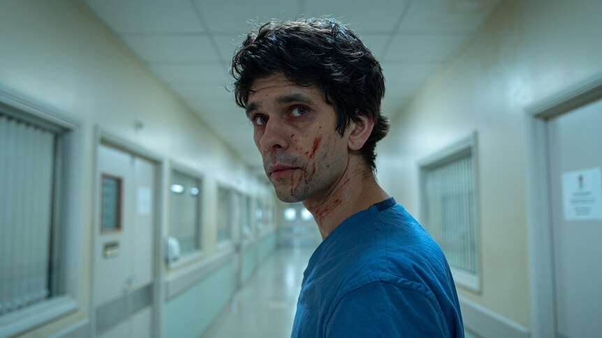 A TV still of Ben Whishaw. He's turning to look down a hospital corridor behind him, and has blood splattered on his face.