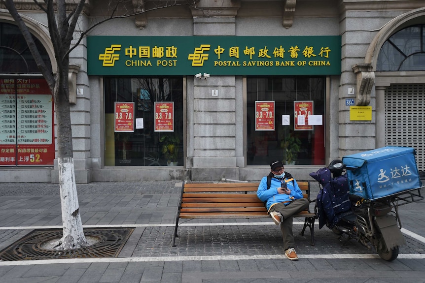 A delivery worker checks his mobile phone outside a Postal Savings Bank of China branch in Wuhan.