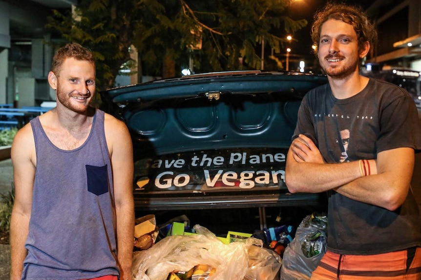 Andy Paine and Franz Dowling stand in front of an open car boot full of bags of food fished out of dumpsters