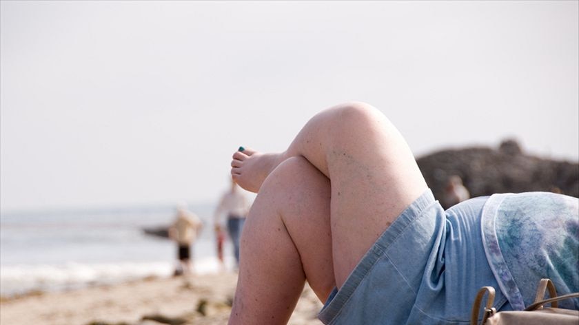 An overweight woman lying a on beach.