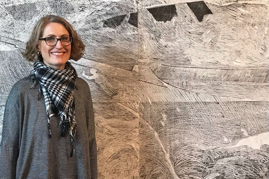 Medium close up of a white woman smiling at the camera in black and white clothing with a black and white etching behind her