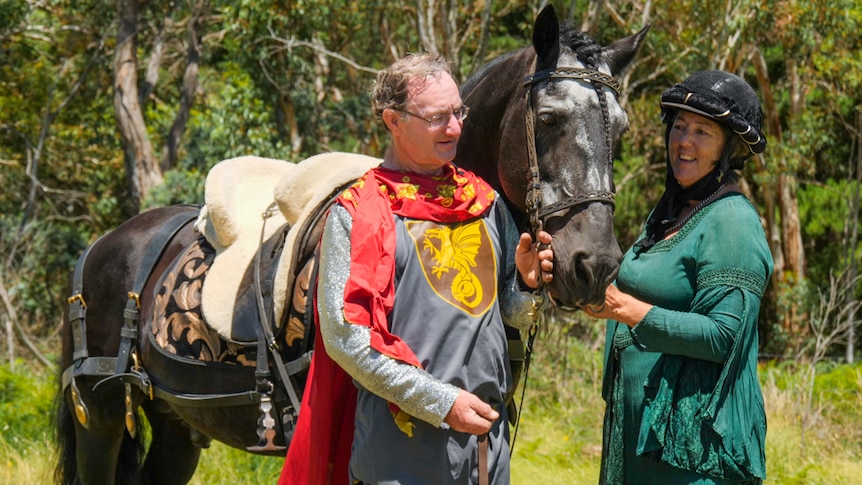 Man and woman dressed in medieval costumes standing with black horse.