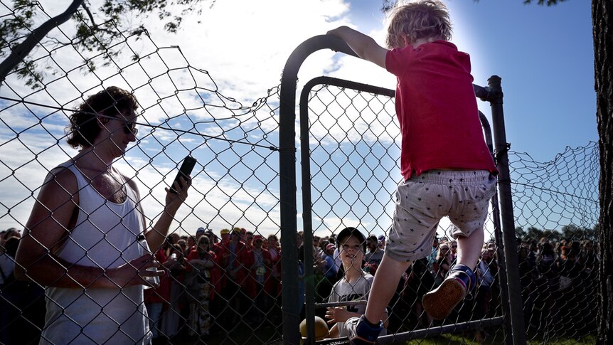 A young boy scales the event fence to re-join his dad after escaping the big line waiting to get in.