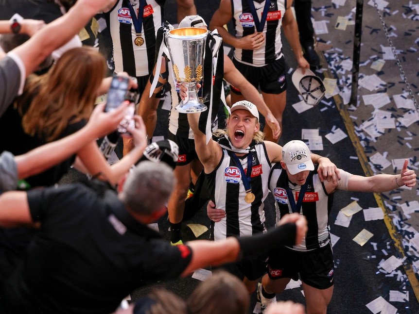 Darcy Moore holds the cup up towards Collingwood fans as he walks down the race