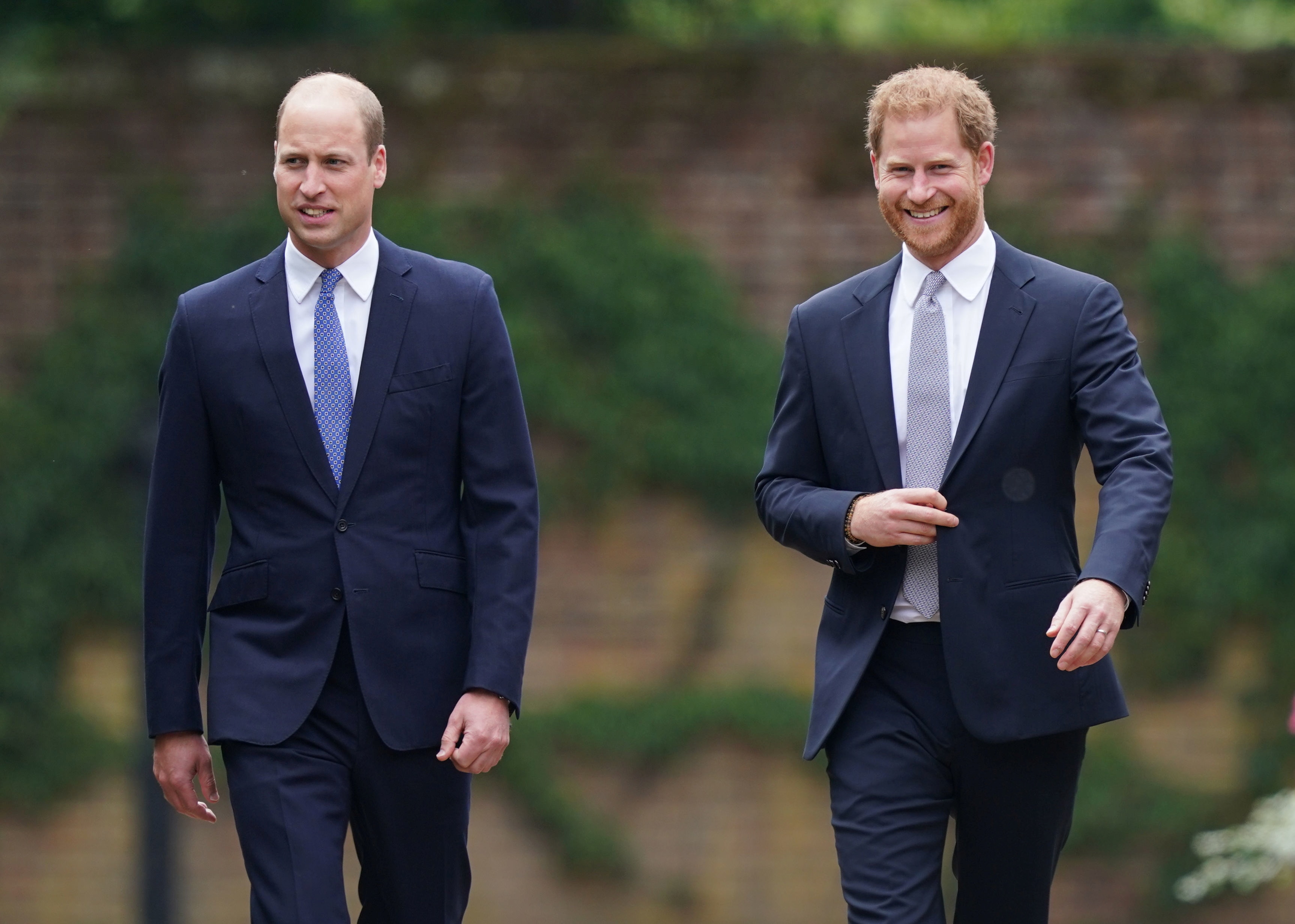 Prince William and Prince Harry smile as they walk alongside each other.