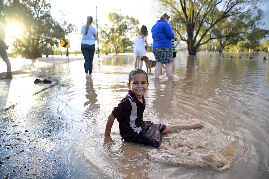 A child sits in floodwaters smiling for camera.