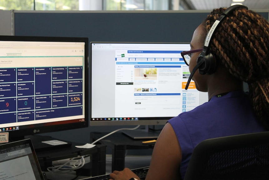 A woman wearing a headset sits at a computer screen.