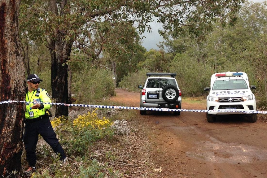 A police car and a four-wheel-drive parked on a bush track, with an officer tying police tape to a tree.