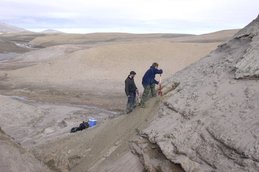 Two scientists digging into large grey hill