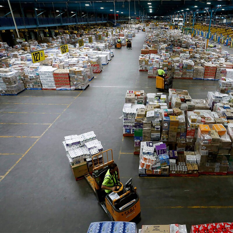 A wide photo taken from an elevated position shows a man driving a forklift in a huge warehouse.