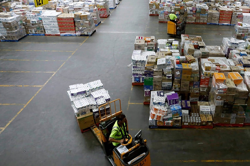 A wide photo taken from an elevated position shows a man driving a forklift in a huge warehouse.