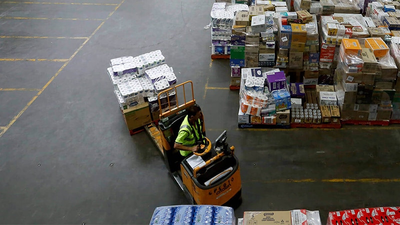 A wide photo taken from an elevated position shows a man driving a forklift in a huge warehouse.
