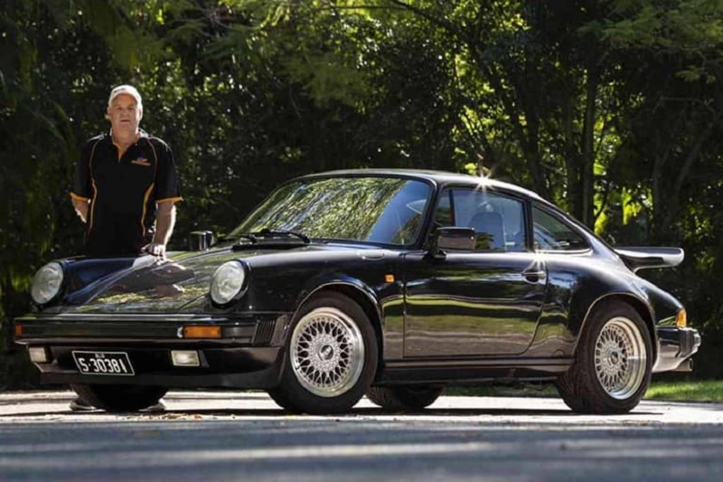 Man in black shirt outside, standing next to black Porche