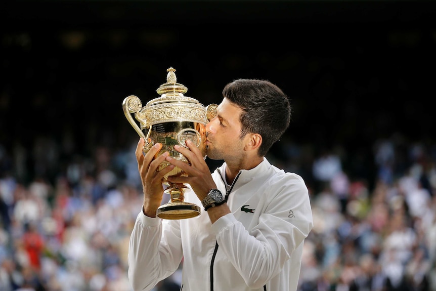Novak Djokovic leans in to kiss the Wimbledon trophy after winning the men's final