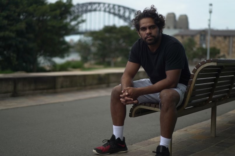 Indigenous man sitting on a bench with the Sydney Harbour Bridge in the background.