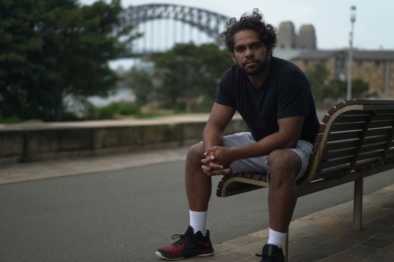 Homme autochtone assis sur un banc avec le Sydney Harbour Bridge en arrière-plan.