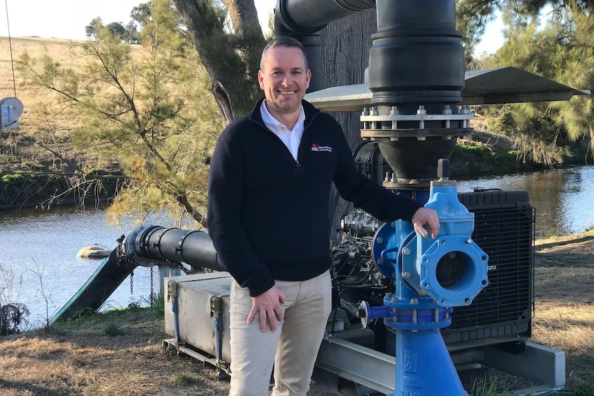 A man stands next to a water pump.