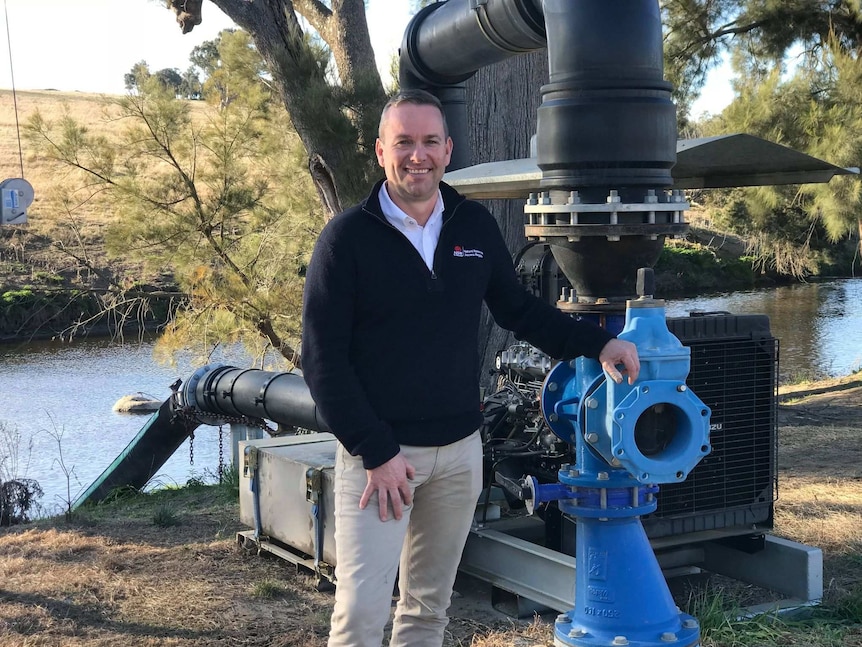 A man stands next to a water pump.