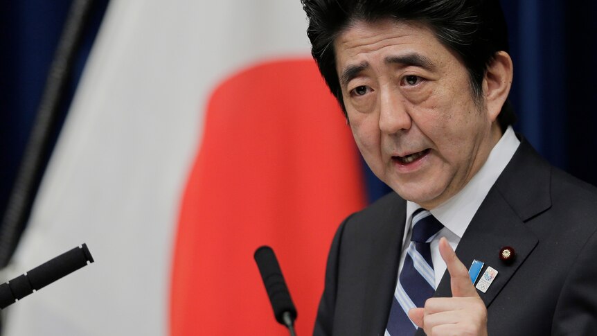 A close up of Abe with the red circle of a Japanese flag in the background