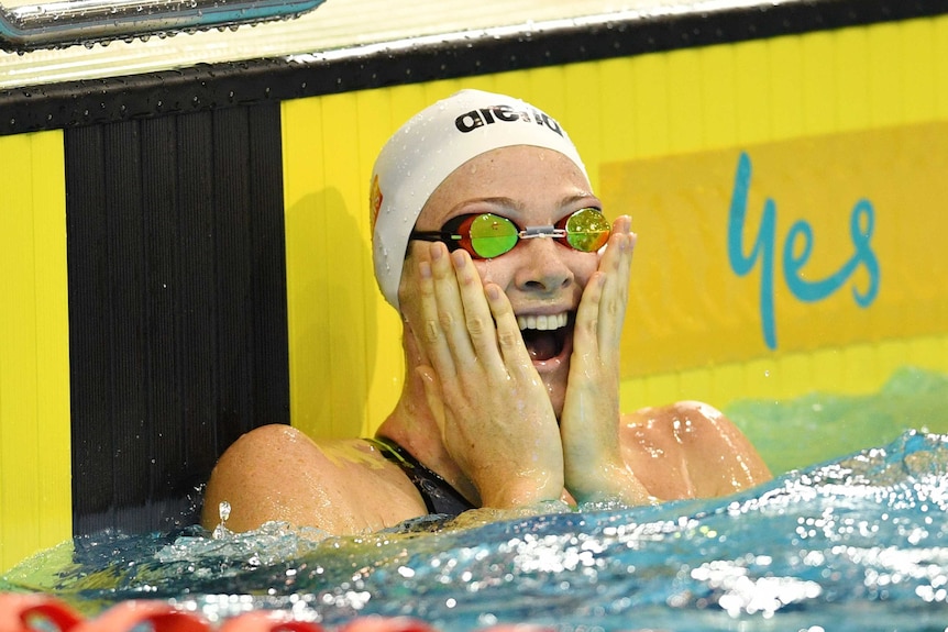 Cate Campbell with goggles and a swimming cap on holds her hands to her face in the pool.