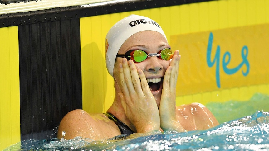 Cate Campbell with goggles and a swimming cap on holds her hands to her face in the pool.