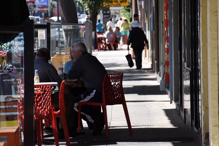 People sit at a table outside a cafe in Preston. Others walk down the street in the background.