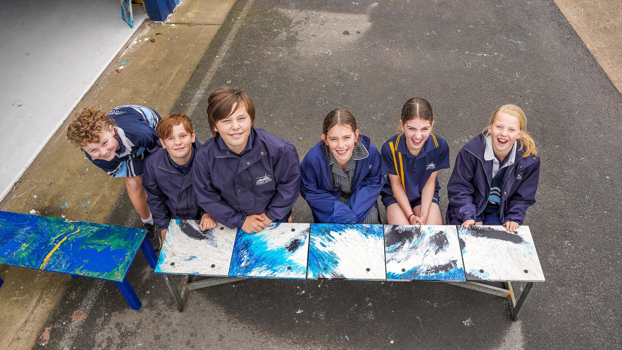 Six primary school aged children lean against a bright blue bench smiling.