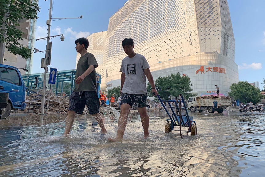 Due giovani uomini in maglietta e pantaloncini con i capelli neri che camminano nell'acqua dell'alluvione