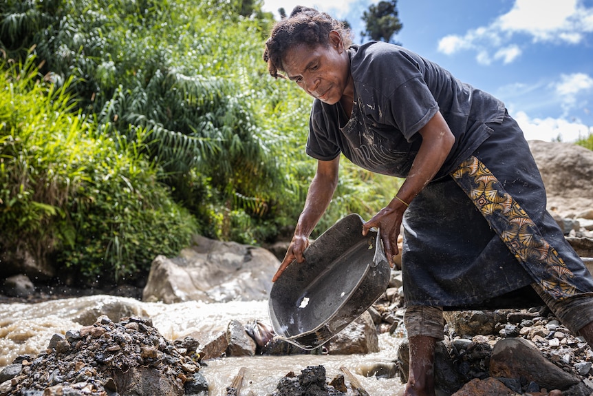A woman holding a metal pan over a river