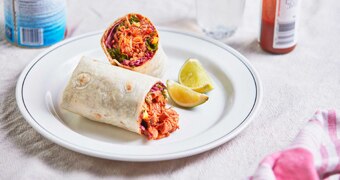 Chicken tinga burrito with kale and corn slaw cut in half and on a plate with lime, a family friendly Mexican dinner recipe.