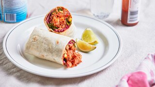 Chicken tinga burrito with kale and corn slaw cut in half and on a plate with lime, a family friendly Mexican dinner recipe.