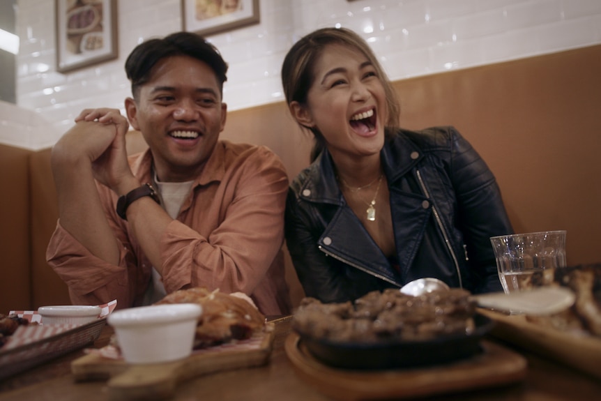 A picture of two people smiling with food on table in front of them.