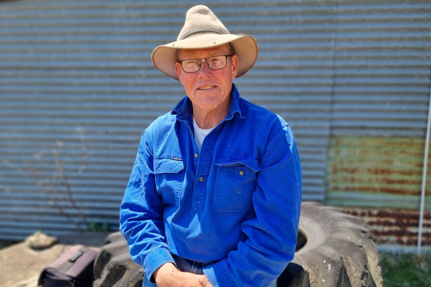 A man in  hat and blue shirt sits on a black tyre.