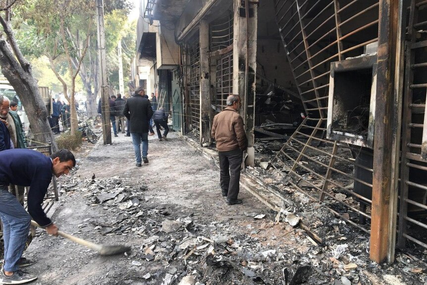 Iranians walk past a charred bank that was set ablaze by protesters during a demonstration,