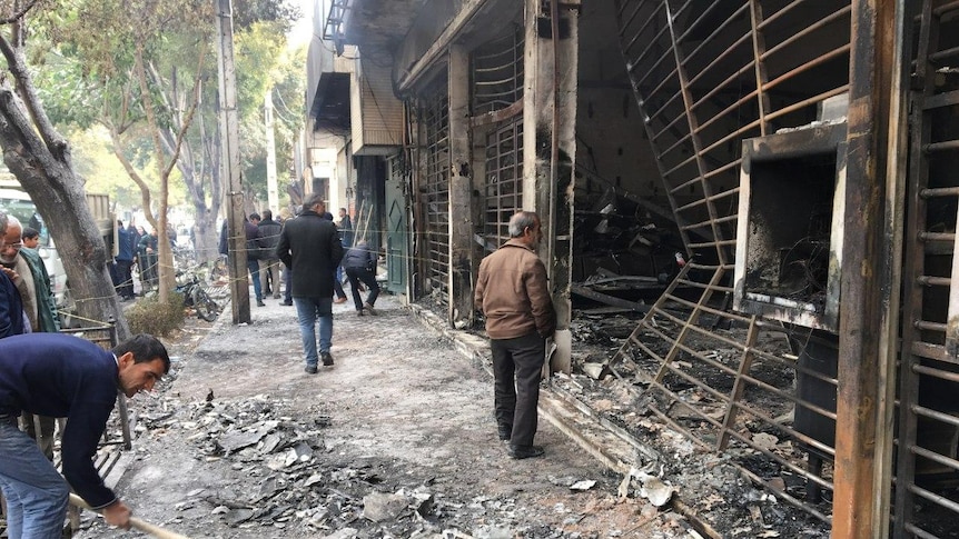 Iranians walk past a charred bank that was set ablaze by protesters during a demonstration,