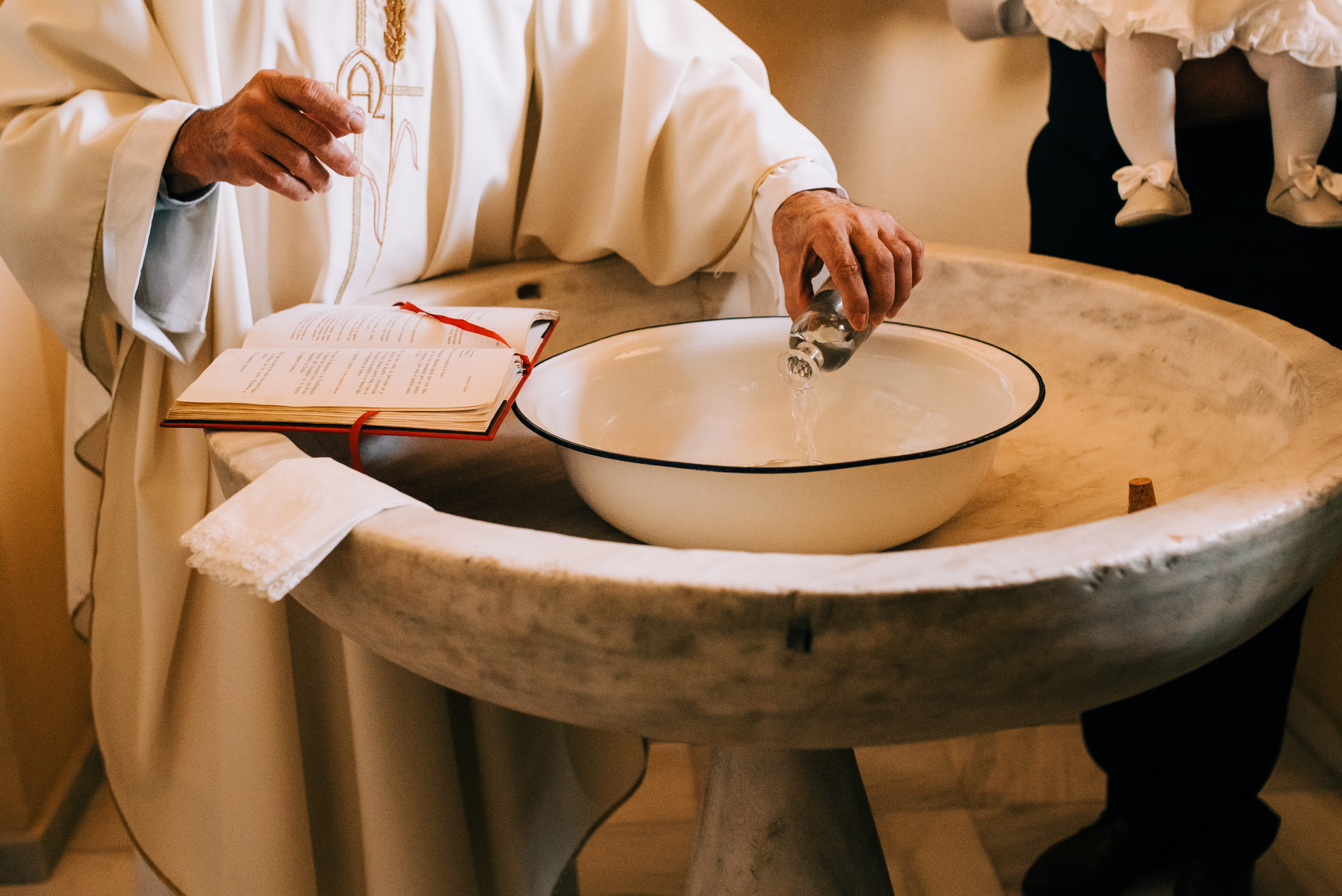 hands of priest in white robe pouring water into baptismal font