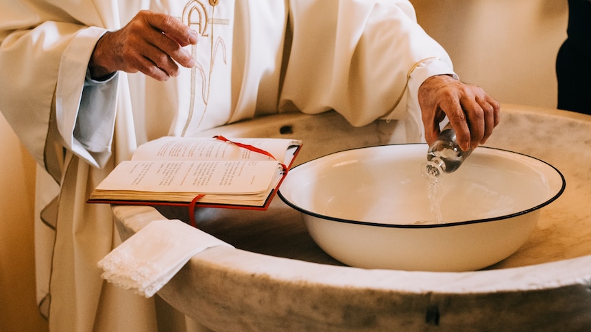 hands of priest in white robe pouring water into baptismal font