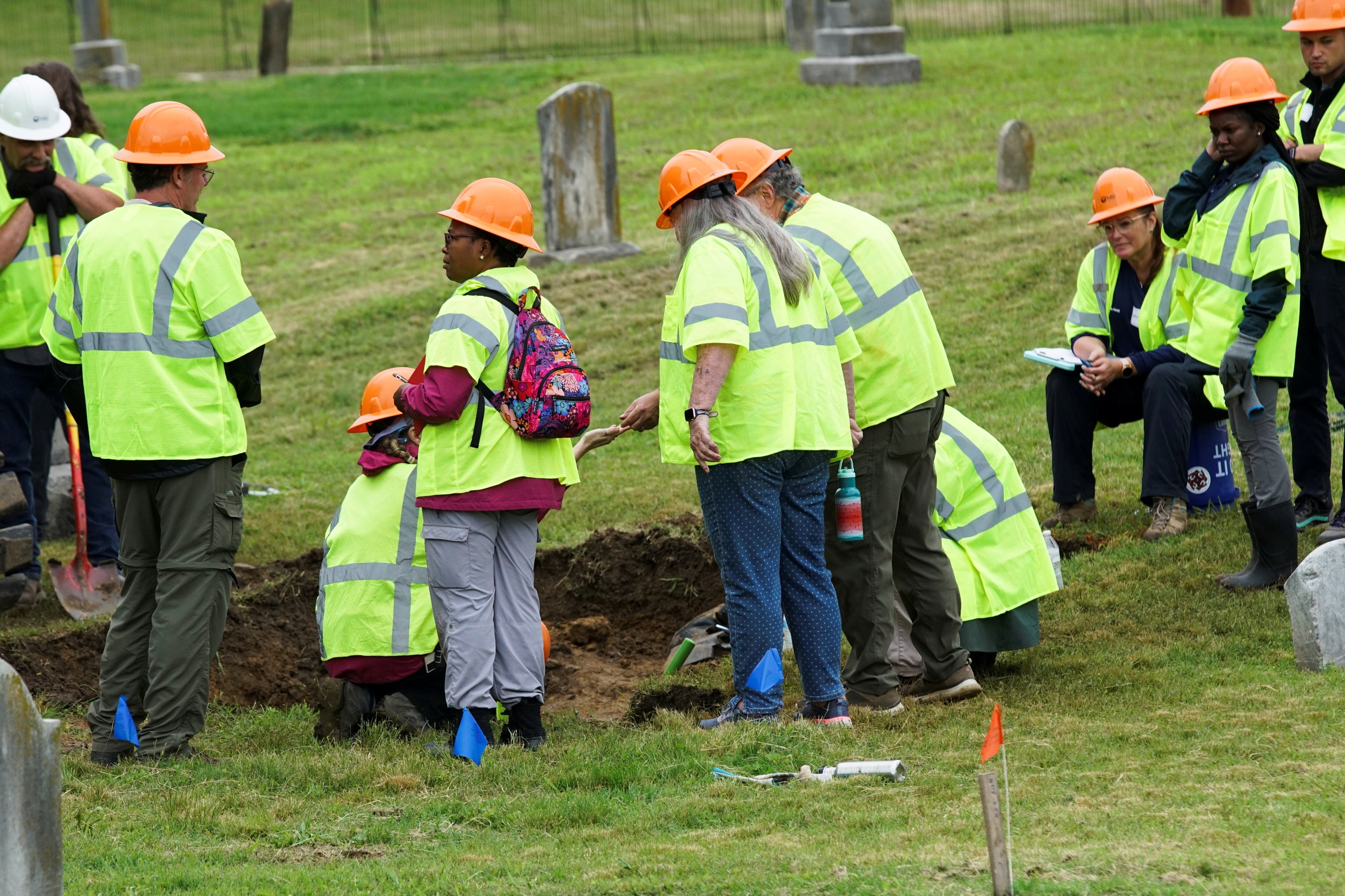Un grupo de personas con cascos naranjas y chalecos de seguridad excavan en una tumba