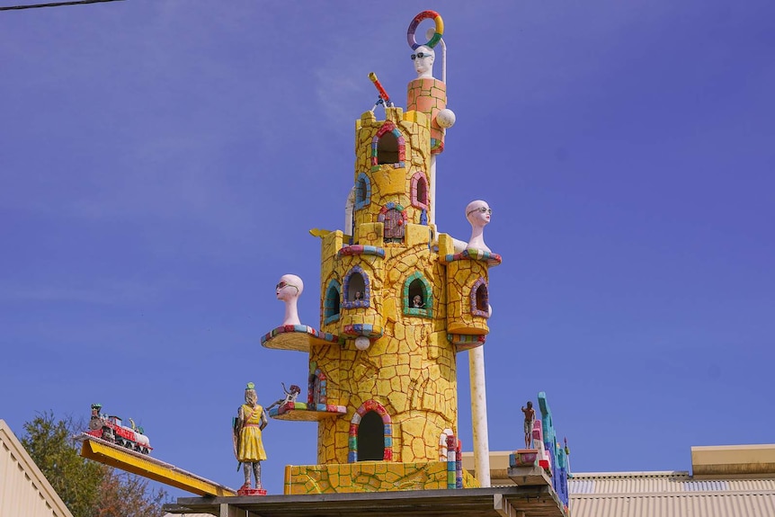A large model yellow fairy castle decorated with polystyrene heads wearing sunglasses and red lipstick.