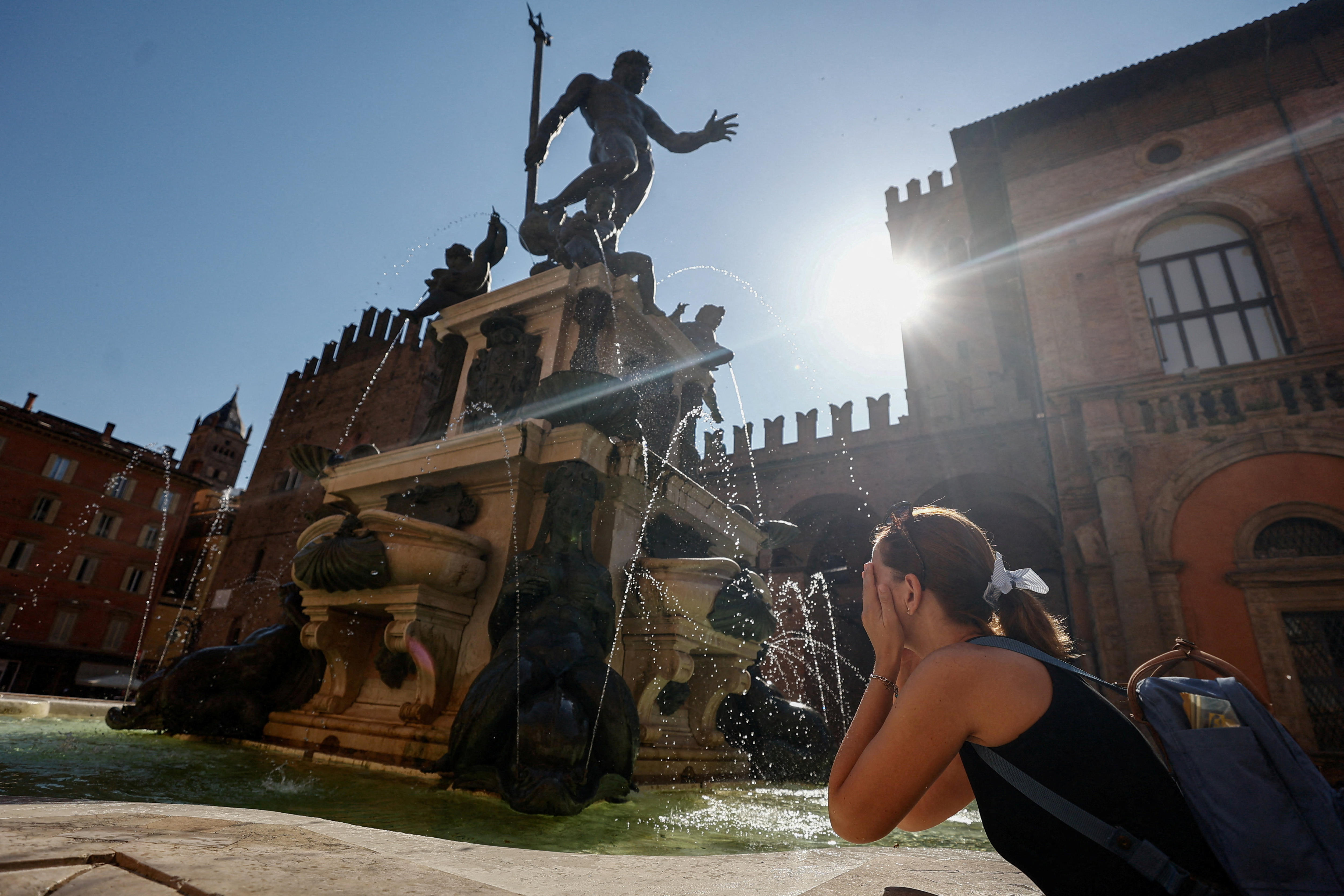A woman splashes water on her face from a large fountain in the shape of Neptune.