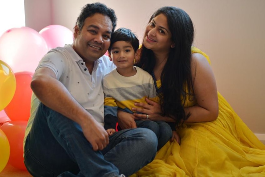 Dipti Ray and her husband sit on the floor with their son between them surrounded by birthday balloons. 