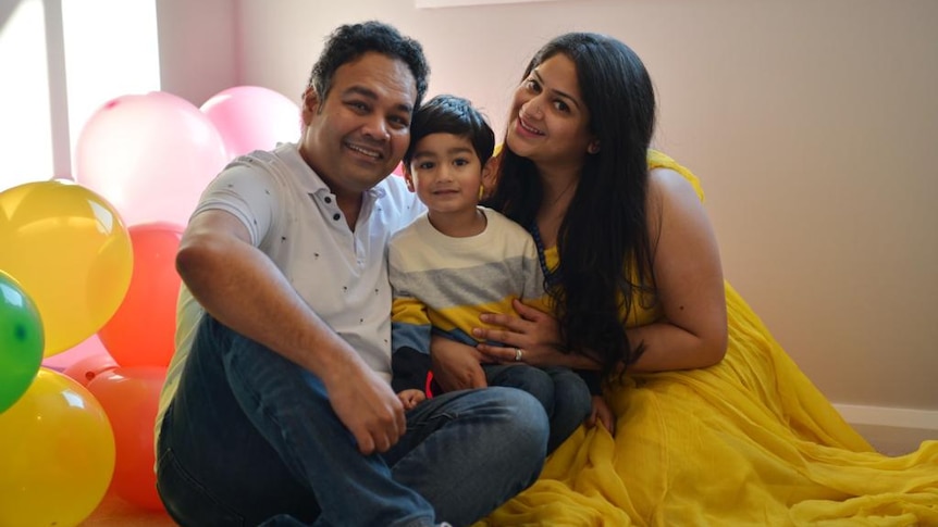 Dipti Ray and her husband sit on the floor with their son between them surrounded by birthday balloons. 
