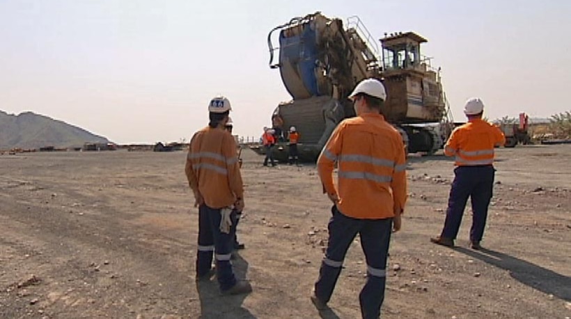 Three workers stand in high res outfits in front of heavy machinery with their backs to the camera