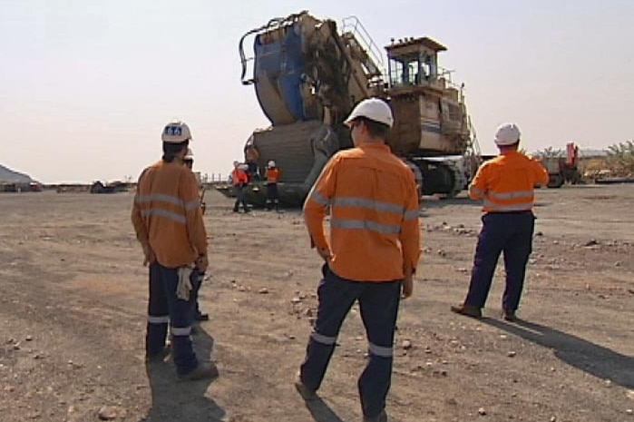 Three workers stand in high res outfits in front of heavy machinery with their backs to the camera