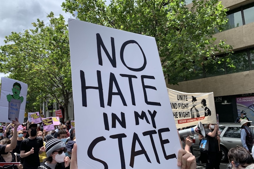 A sign that says 'no hate in my state' in black that's held up by a protester. 