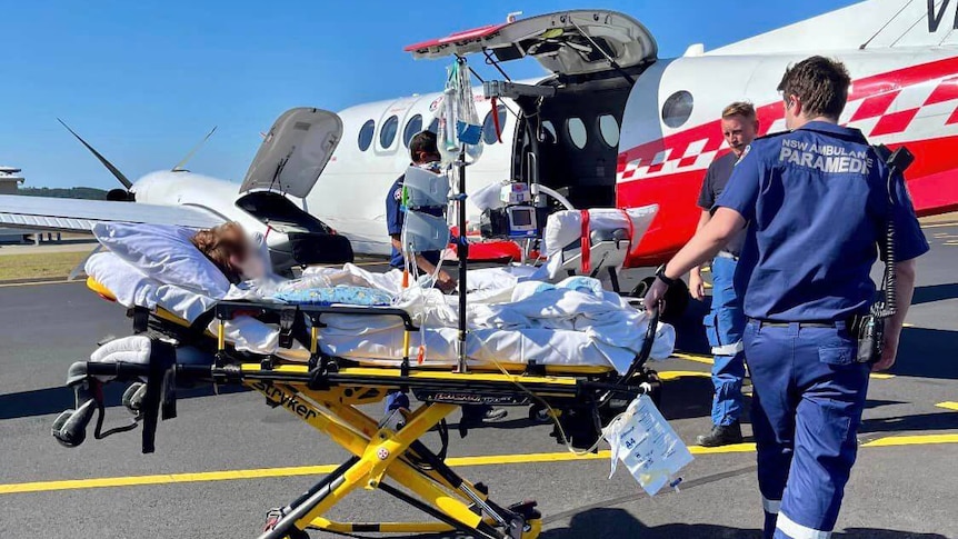 ambulance workers with a patient standing next to a helicopter about to load the person into the aircraft