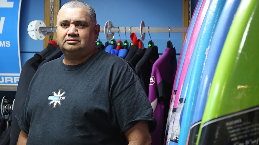 Surf shop owner Richard Beckers stands next to a row of surf boards.