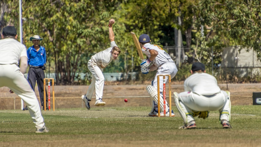 A bowler is mid action and the ball about to hit the pitch as a batsman and wicketkeeper prepare