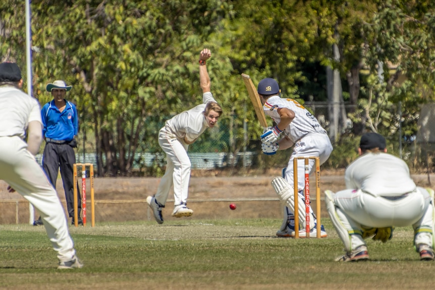 A bowler is mid action and the ball about to hit the pitch as a batsman and wicketkeeper prepare