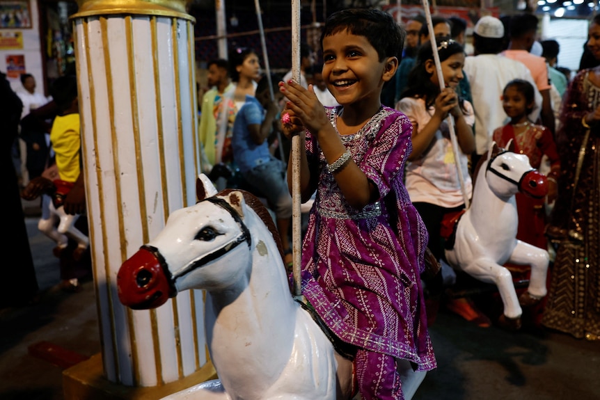 A thin young girl rides a white horse on a carousel.